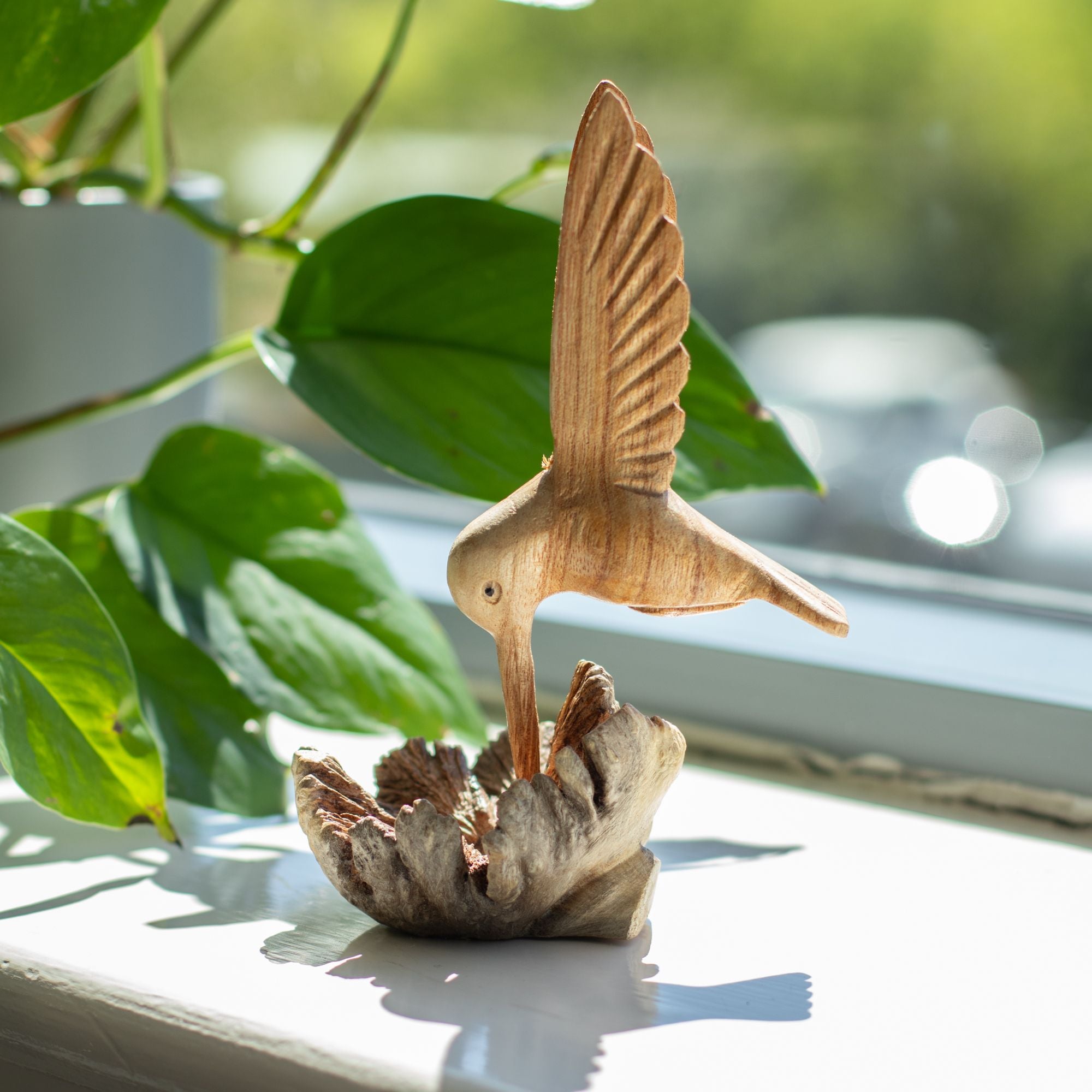 Escultura hecha a mano de un colibrí bebiendo néctar de un nudo de madera