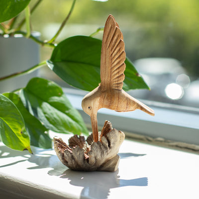 Escultura hecha a mano de un colibrí bebiendo néctar de un nudo de madera