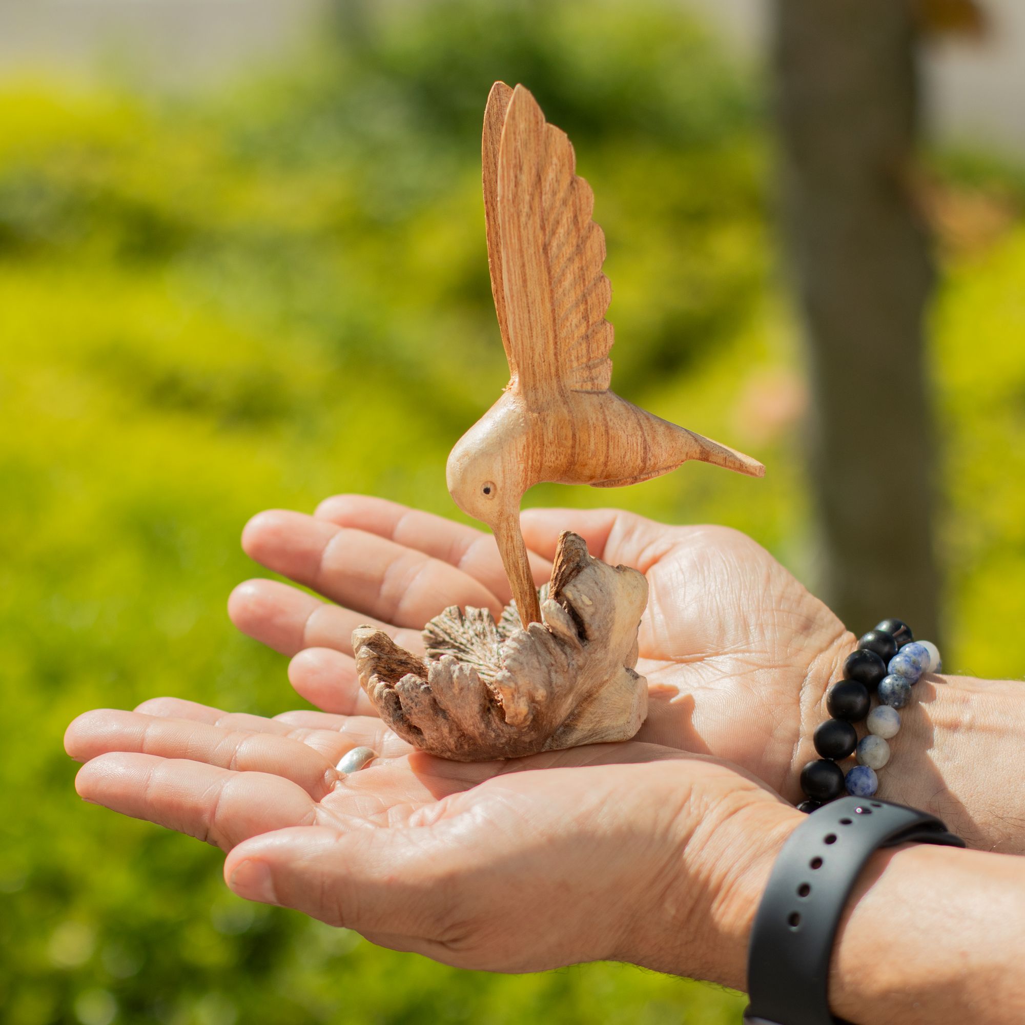Escultura hecha a mano de un colibrí bebiendo néctar de un nudo de madera